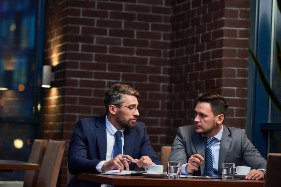Deux hommes d'affaires en costume cravate discutent sérieusement autour d'une table dans un restaurant.