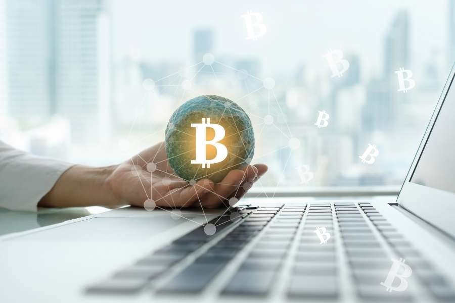 Une main tenant une sphère verte avec un logo Bitcoin devant un ordinateur portable, symbolisant l'automatisation de ses investissements en crypto.