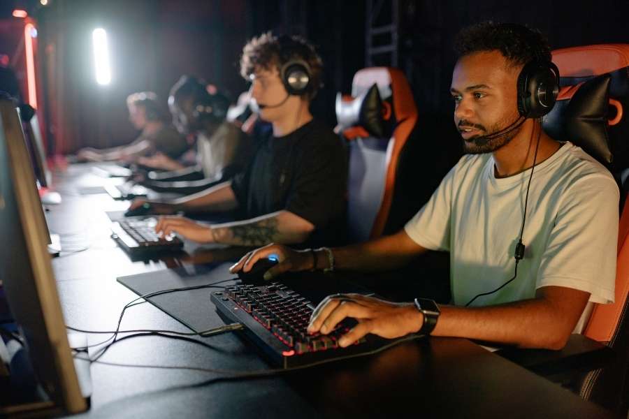 Des joueurs concentrés jouent en réseau sur des PC de bureau équipés de casques audio et de claviers lumineux.